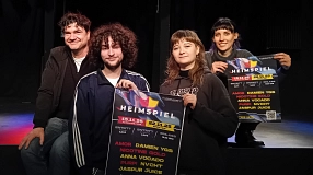 Vier Personen posieren auf einer Bühne mit einem Plakat zum Musikfestival „Heimspiel“ im Alten Schlachthof in Stade. Zwei der Personen halten das bunte Veranstaltungsplakat gut sichtbar in die Kamera. Auf dem Plakat stehen Termine, Musikrichtungen und Künstler*innennamen.&nbsp;&copy;&nbsp;Hansestadt Stade