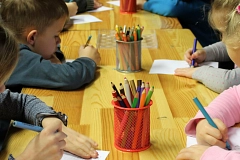 Kinder sitzen sich gegenüber an einem langen Tisch und malen