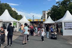 Sommerfest im Altländer Viertel 2025 Menschen unterschiedlicher Altersgruppen besuchen ein Sommerfest im Stadtteil. Zwischen weißen Pagodenzelten bewegen sich Erwachsene und Kinder, einige Kinder spielen oder fahren mit einem Spielzeugauto. Im Hintergrund sind Bäume und ein mehrstöckiges Wohnhaus zu sehen. Die Atmosphäre ist lebendig und einladend.