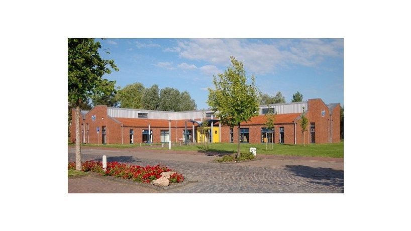 Die Stadtbibliothek Stade bei blauem Himmel von außen fotografiert. Im Vordergrund sind kleine Bäume und ein Beet mit rot blühenden Blumen zu sehen&nbsp;&copy;&nbsp;Hansestadt Stade