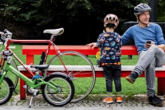 Ein Mann und sein Sohn machen es sich bei einer Parkbank bequem. Neben ihnen stehen, an die Bank gelehnt, ihre Fahrräder